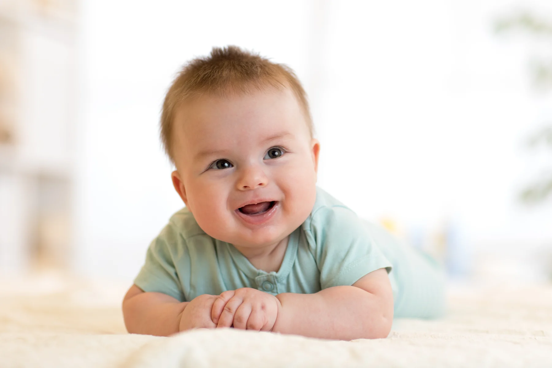 A baby smiling while lying on their tummy.